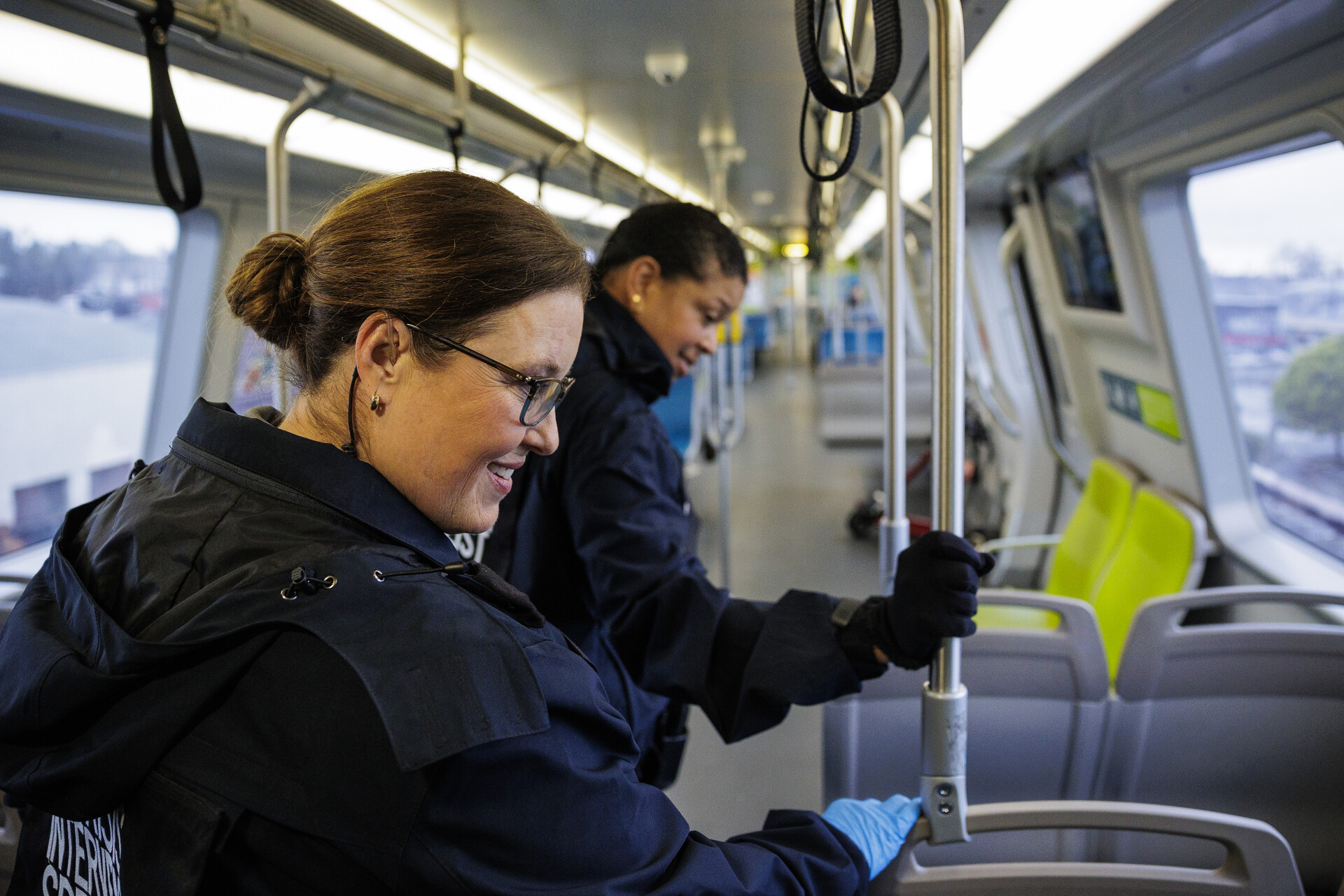 Two middle-aged women in dark-blue uniforms speak to an unseen passenger on a BART train.