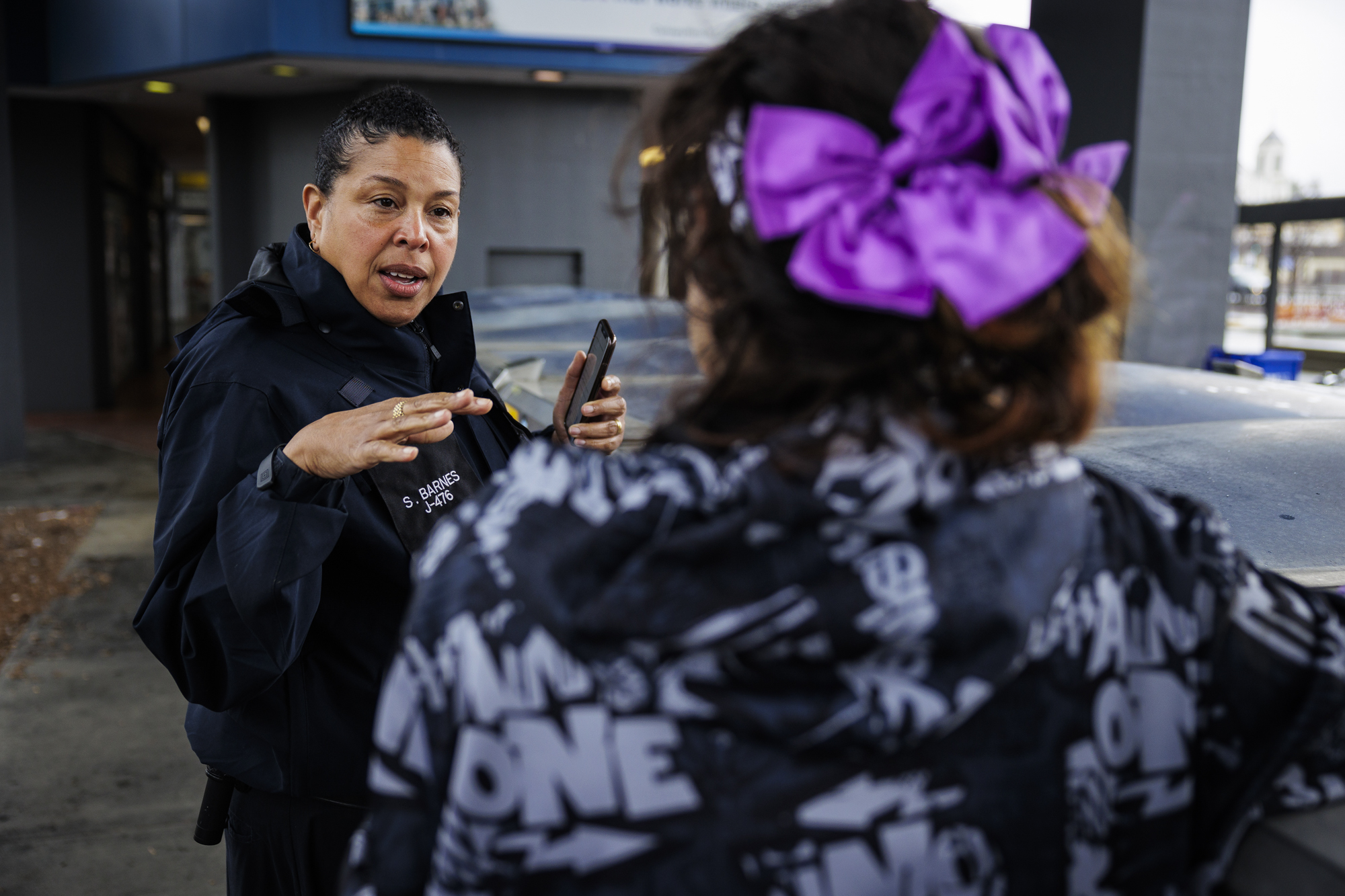 A middle-aged Black woman speaks to a younger woman wearing a purple hair decoration.
